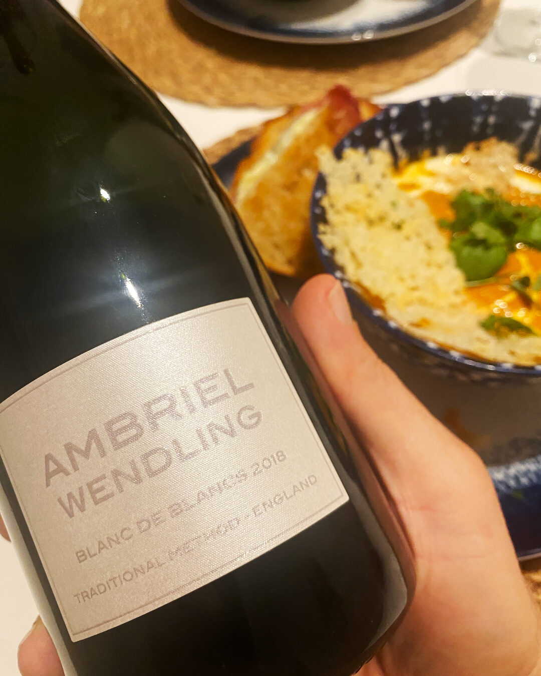 Close-up of an Ambriel Wendling Blanc de Blancs 2018 bottle held in front of dinner.