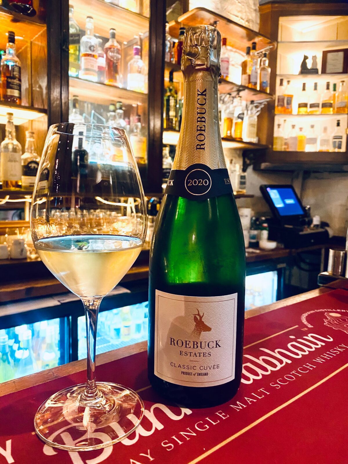 A glass of Roebuck Estates Classic Cuvée 2020 beside the bottle at The Wee Whisky Bar in Glasgow.